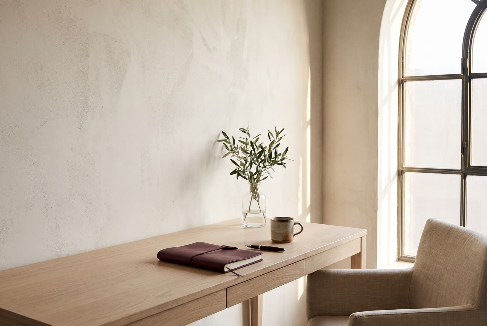 A calm office corner with a burgundy notebook, a pen and coffee in morning light