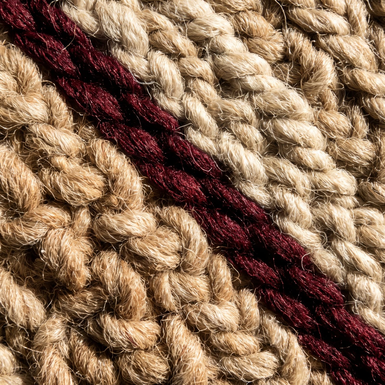 Macro detail of hand tufted wool pile with a burgundy band